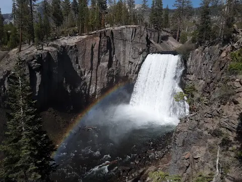 A large waterfall flowing over rocky cliffs with a rainbow in the mist below.