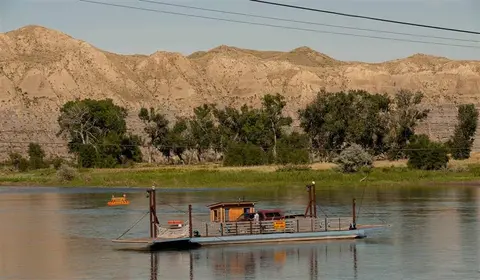 A ferry on a river with mountains and trees in the background.