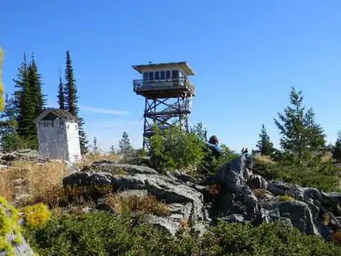 A fire lookout tower stands on a rocky mountain summit.