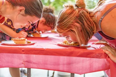 People participate in a pie-eating contest outdoors.