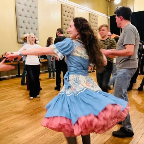 People dancing indoors on a wooden floor.