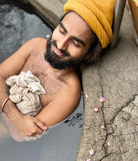A man wearing a yellow turban relaxes in a pool with flowers nearby.