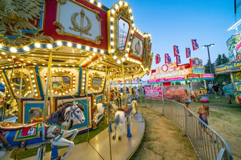 A brightly lit carousel at an outdoor fair or carnival at dusk.
