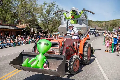 A tractor decorated with alien figures and a spaceship drives down a street during a parade.