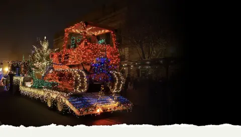 A large tractor decorated with Christmas lights is parked at night.