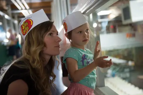 A woman and a young girl wearing paper hats look through a window.