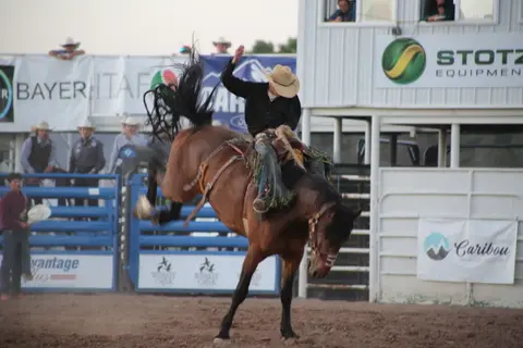 A cowboy rides a bucking horse at a rodeo arena.