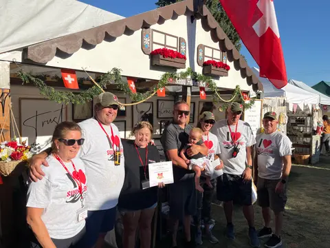 A group of people pose in front of a decorated booth at an outdoor event.