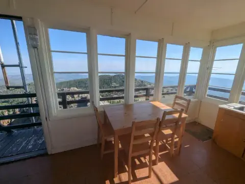 The interior of a fire lookout tower with windows looking out over mountains.