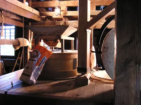 The interior of a wooden mill building with machinery and a bag of grain.