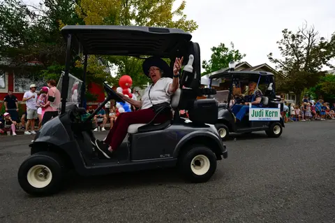 A woman waves from a golf cart during a parade.
