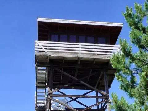 A wooden fire lookout tower stands against a clear blue sky.