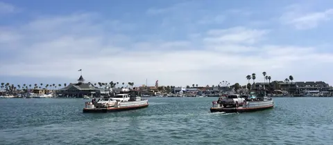 Two ferries carrying cars across a harbor with buildings in the background.