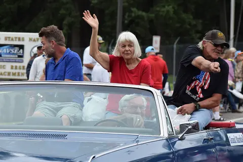 People riding in a convertible car during a parade.