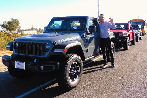 A person standing beside a gray Jeep Rubicon waving at the camera.