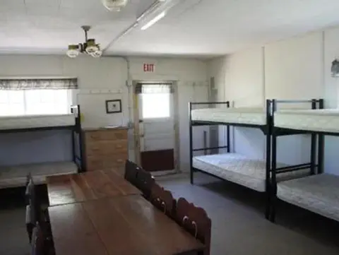 An interior view of a dormitory room with bunk beds and wooden tables.