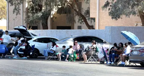 A group of people sitting in chairs along a street next to parked cars.
