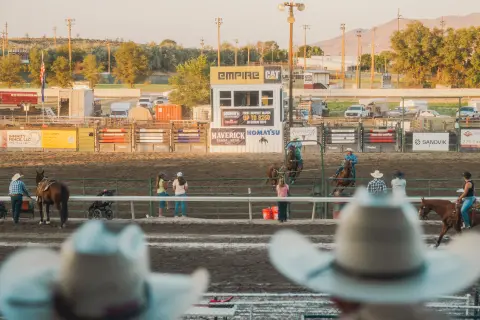 A rodeo arena with people and horses viewed past cowboy hats in the foreground.