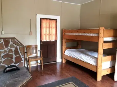 A simple rustic room with a wooden bunk bed and a stone fireplace.