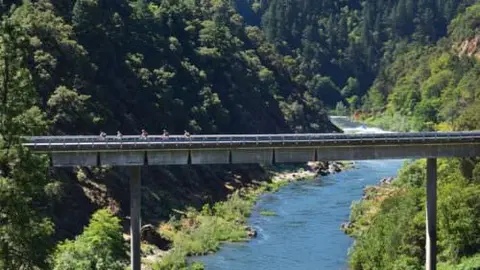 A bridge spans across a river flowing through a heavily forested canyon.