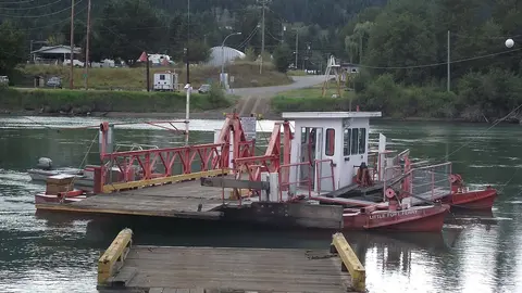 A small ferry floats on a river with a dock in the foreground.