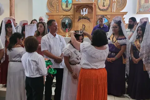 A woman places a crown on a young woman wearing a sash during a ceremony inside a building.