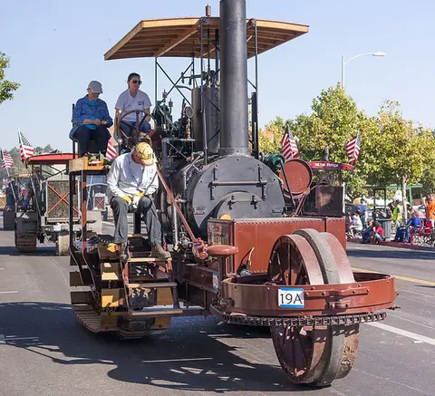 A vintage steam tractor participates in an outdoor parade.