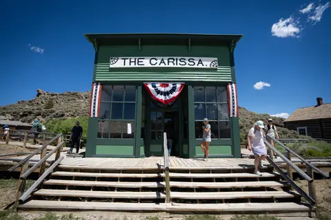 A historic green building named The Carissa with visitors walking around outside.