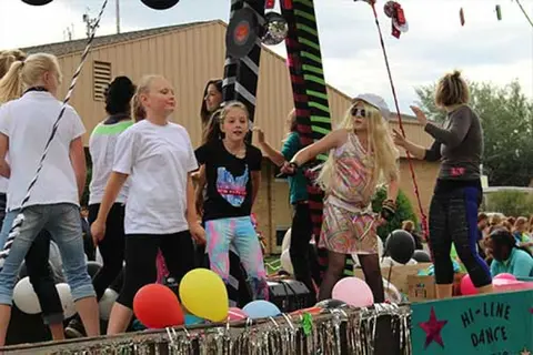 Children and adults dancing on a decorated float outdoors.