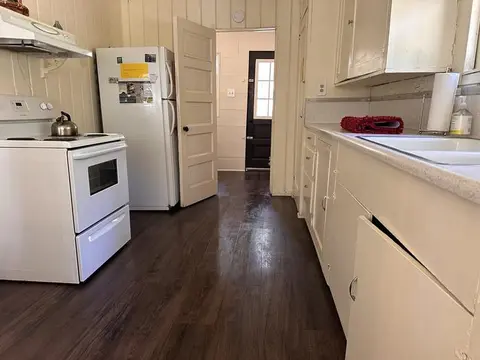 An interior view of a retro kitchen with white appliances and cabinets and dark wood floors.