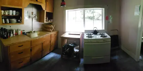 An interior shot of a rustic kitchen with wooden cabinets, a stove, and a window.