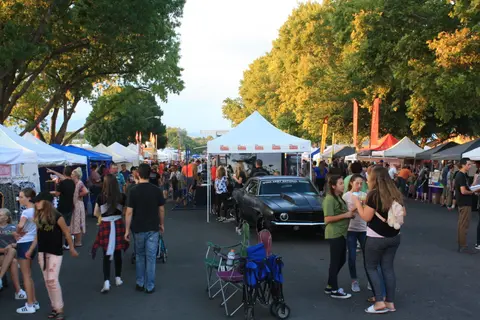 An outdoor street market with people walking among vendor tents and a displayed car.