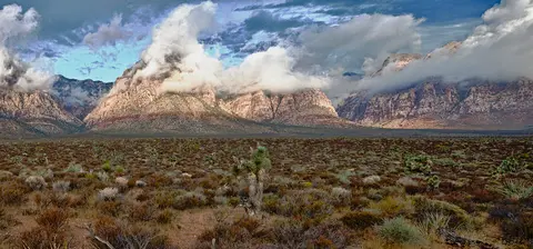 A wide angle landscape of a desert and mountains with clouds.
