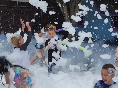 Children play outside in a large pile of soapy foam.