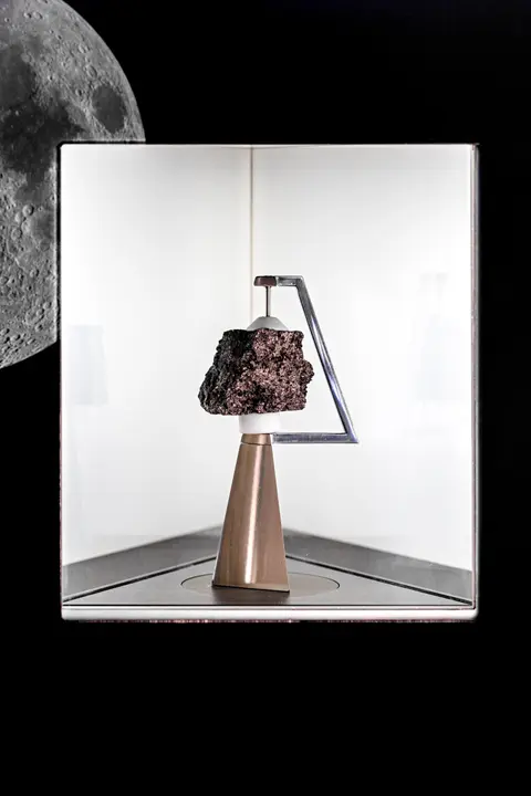 A rock on display inside a lighted case against a dark background with a moon graphic.