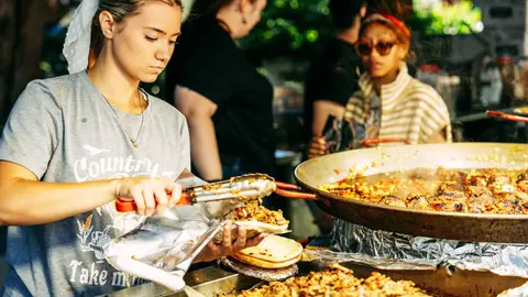 A woman serves food from a large pan at an outdoor event.