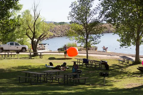 People enjoy a sunny day at a picnic and beach area near a lake.