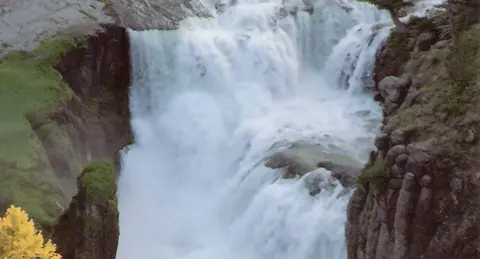 A view of a powerful waterfall flowing between rocky cliffs and green vegetation.