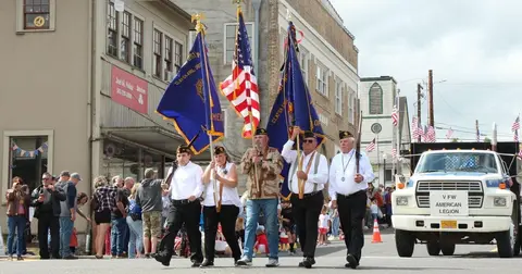 A color photograph of people carrying flags in a parade down a street.