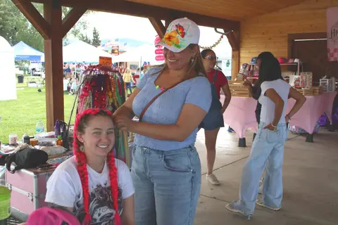 A woman gets her hair braided at an outdoor market stall.