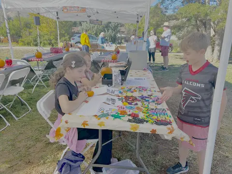 Children selling crafts at a table under a tent outdoors.