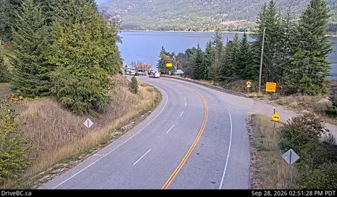 A winding highway curves past a forested hillside toward a body of water.
