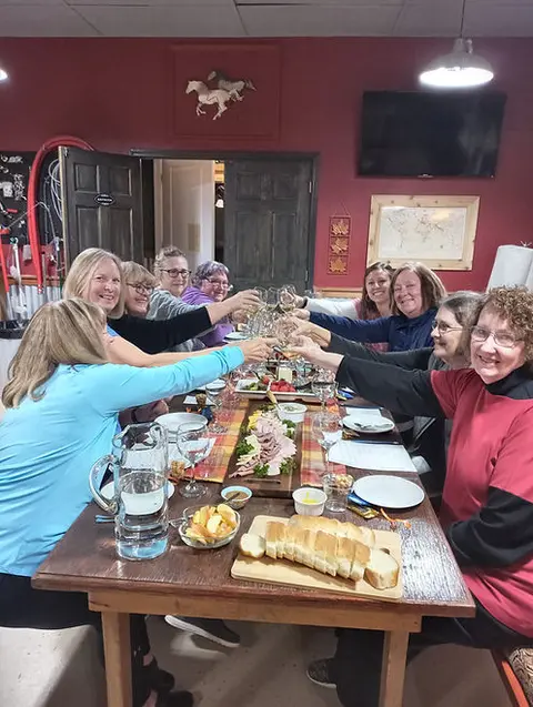 A group of women seated around a long dining table are raising glasses in a toast.