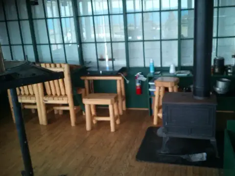 Interior view of a cabin with a wood stove and wooden furniture.