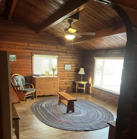 An interior view of a rustic log cabin living room with wooden walls and a braided rug.