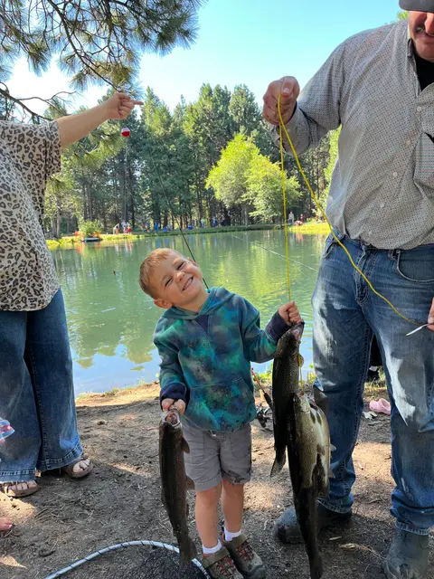 A young boy holds up fish he caught while fishing by a pond.