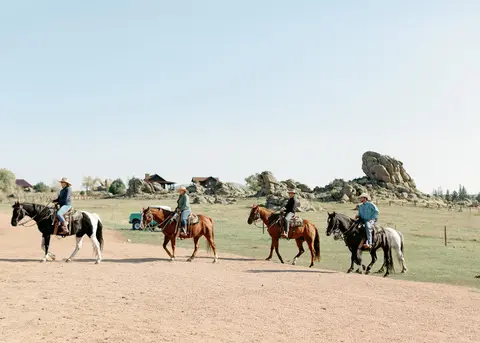Four people ride horses in a line across an open landscape.