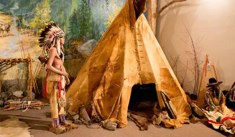 A museum exhibit features a large teepee and mannequins in traditional attire.