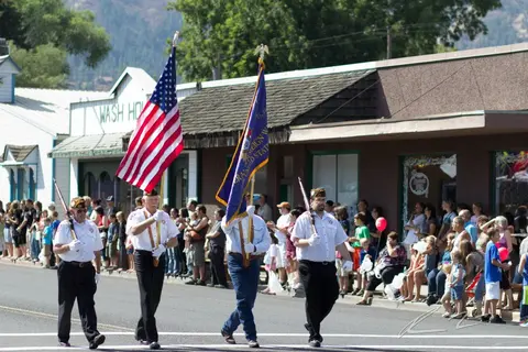 Veterans carry flags and rifles in a street parade.