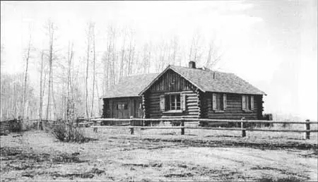 Black and white historic photo showing a log cabin behind a wooden fence.